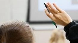 Student raises her h和 in classroom.