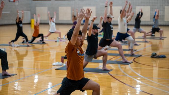 A group of students does yoga in a gym. 他们摆出战士的姿势. 