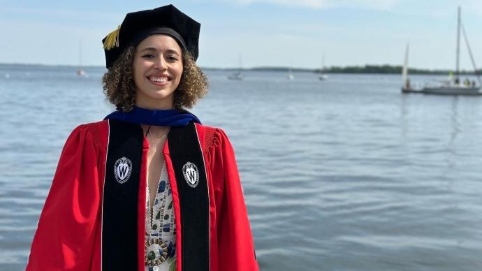 Lauren Wilks stands in front of a body of water wearing her full regalia.