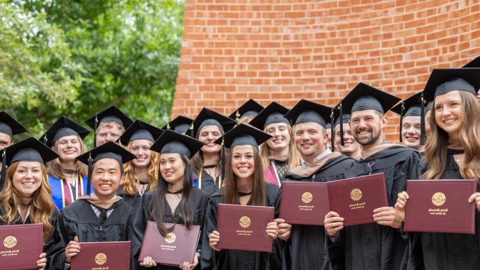 graduates pose for a photo in their caps and gowns in front of Murchison Tower, 持有学位