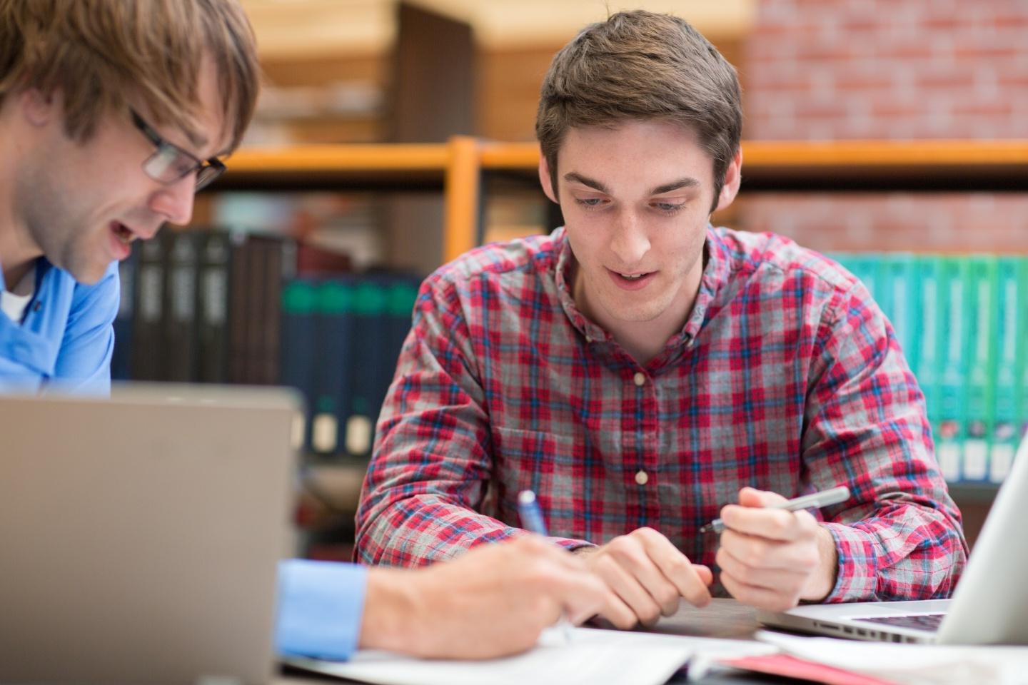 Two students discussing and writing in book