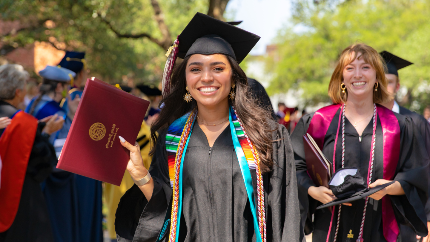 A student smiles while holding their diploma 